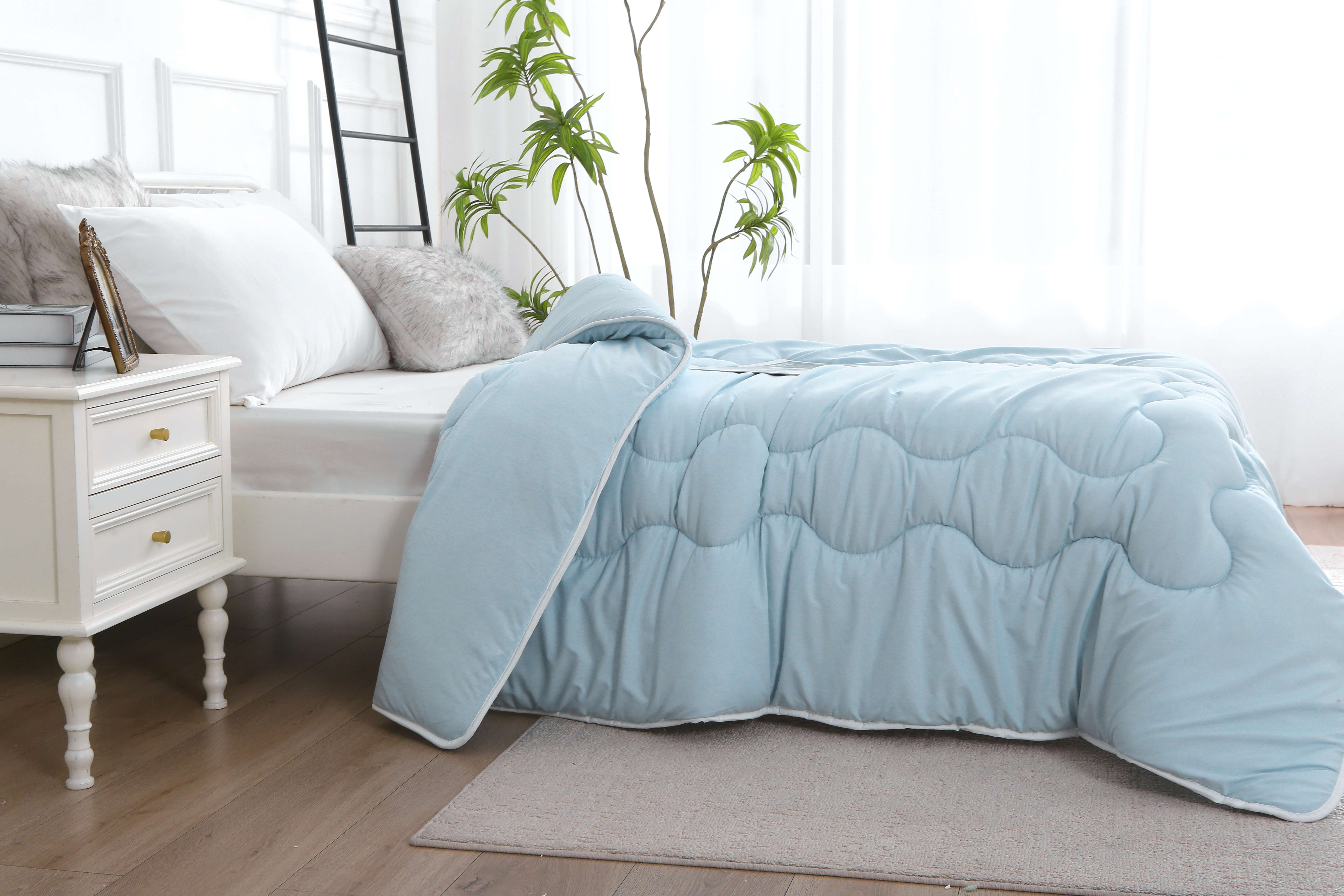 Zijaanzicht van blauw verkoelend zomerdekbed zonder overtrek opgemaakt op bed, licht en ademend voor warme nachten