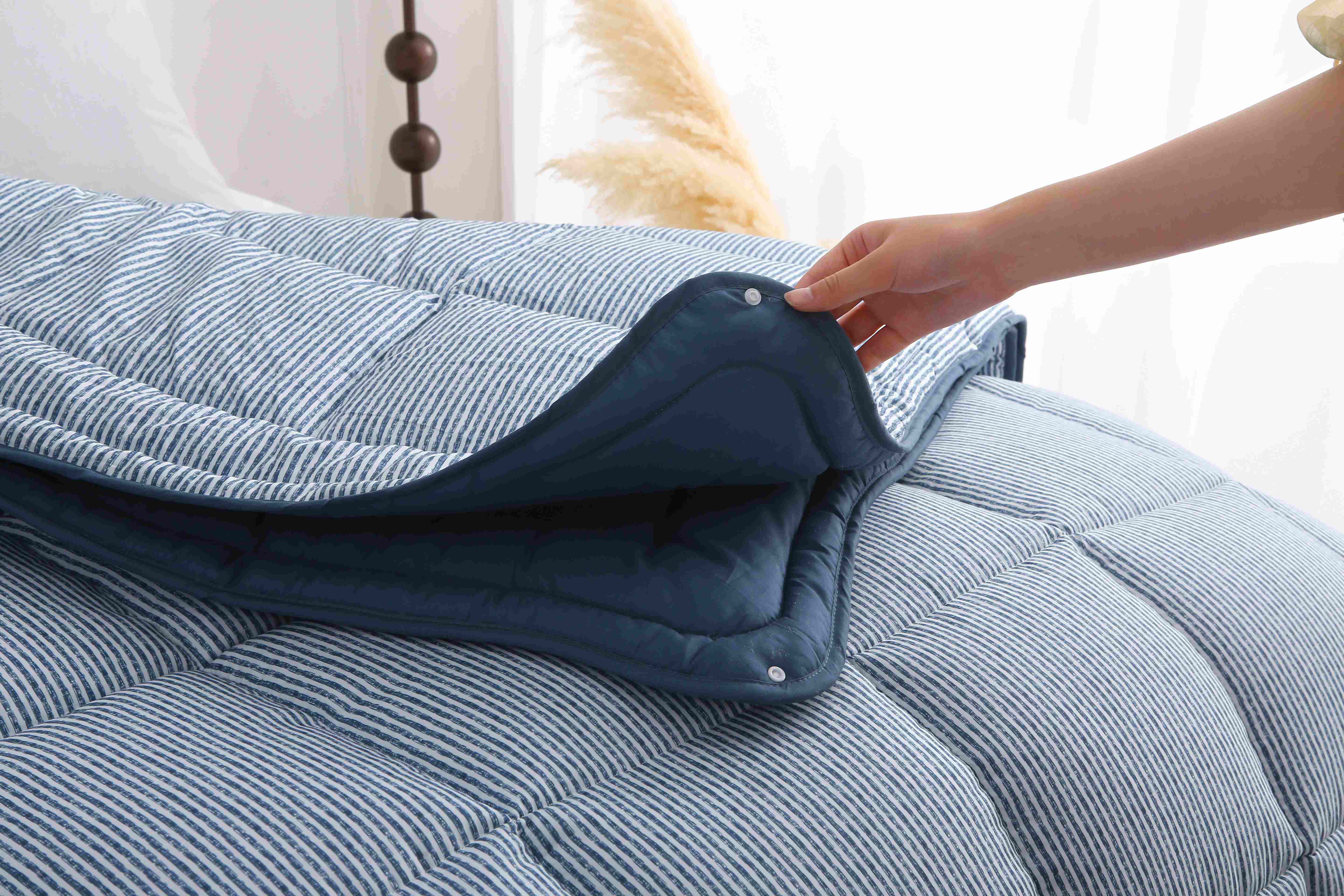 Hand die laat zien hoe de twee delen van het blauw-wit gestreepte 4-seizoenen dekbed aan elkaar worden bevestigd met een drukknop.