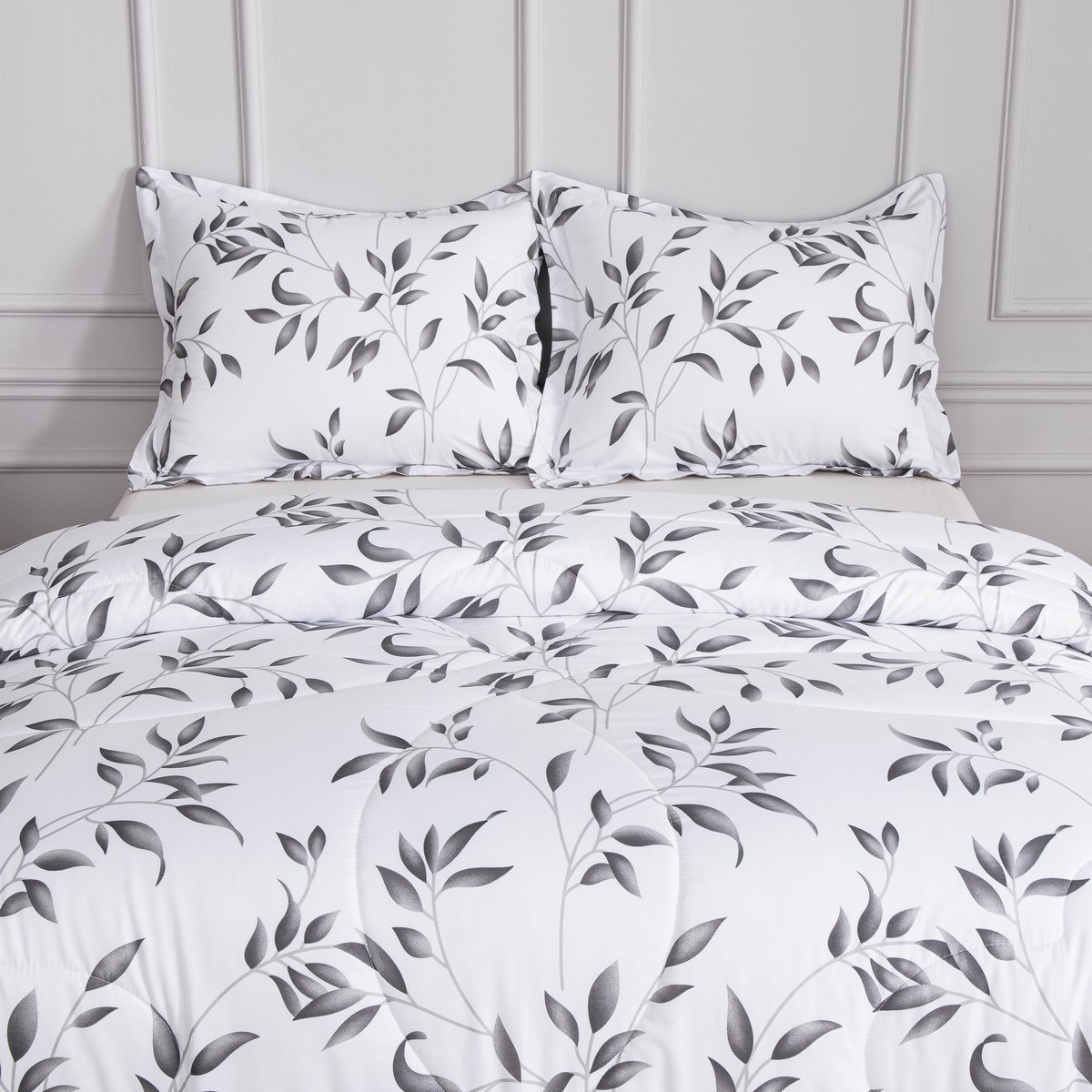 Dichtbij opname van kussens en bovenzijde van het vierseizoenen dekbed Nora met wit‑grijs bladmotief.