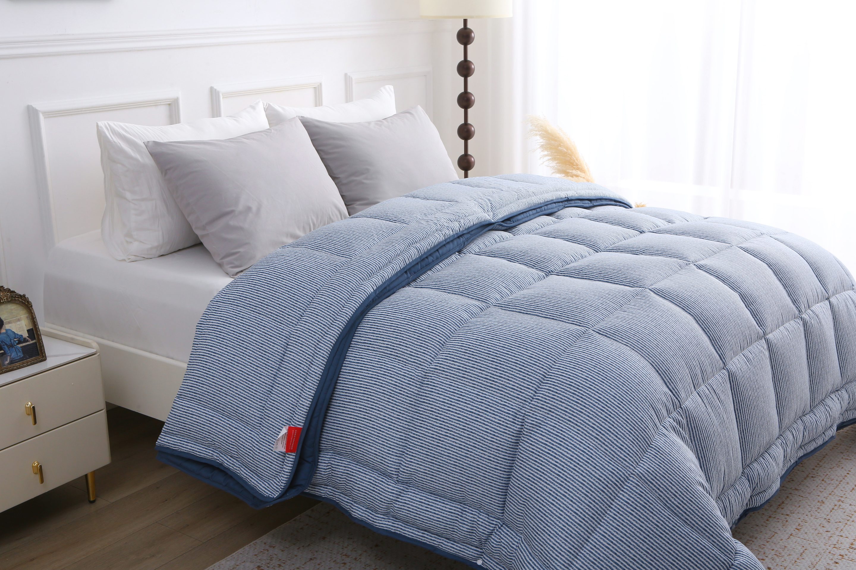 Opgemaakt bed met het blauw-wit gestreepte 4-seizoenen dekbed zonder overtrek, zichtbaar vanuit een zijhoek met lichtinval