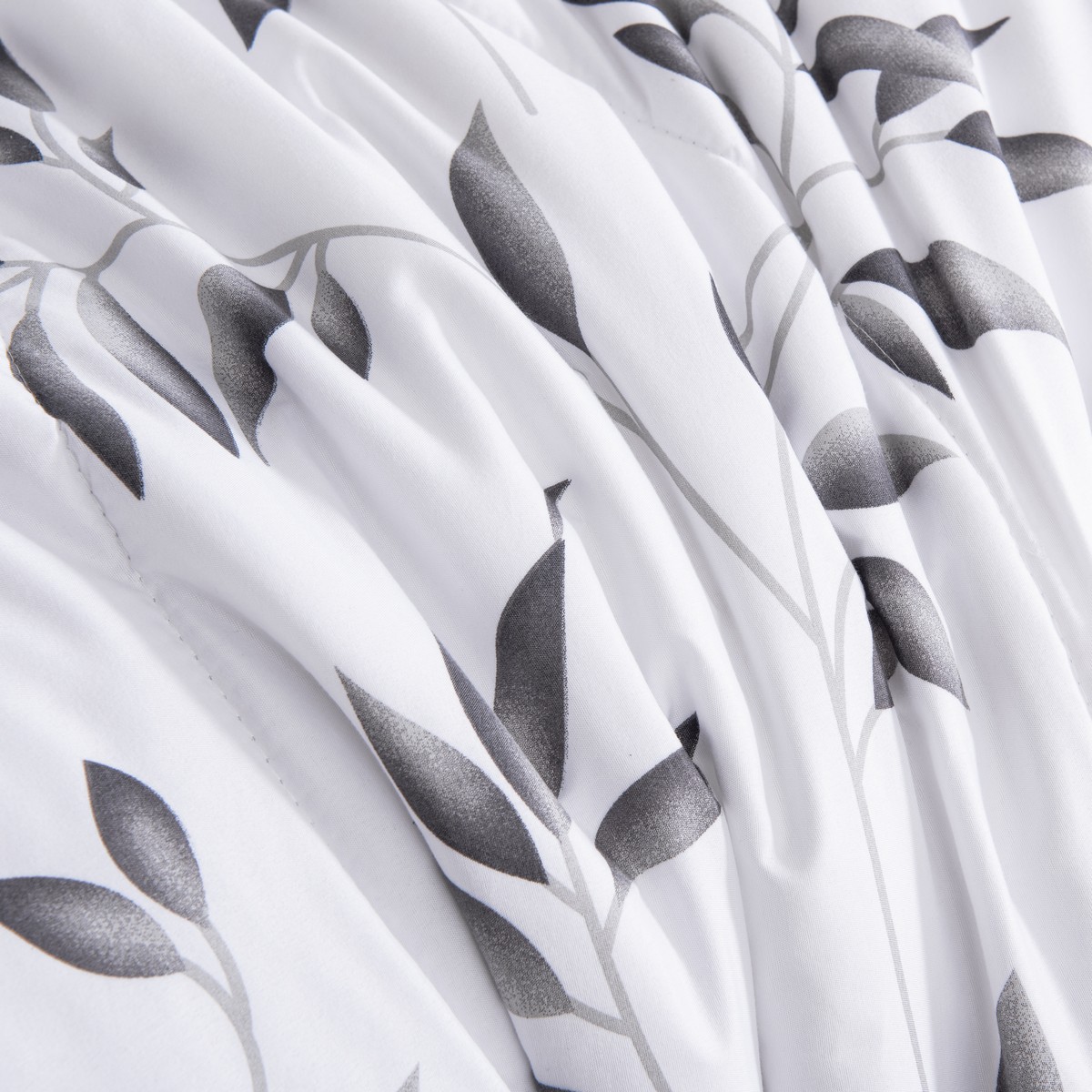 Close‑up van de zachte witte stof van het 4‑seizoenen dekbed Nora met grijze bladeren en vloeiende plooien voor een sierlijke look