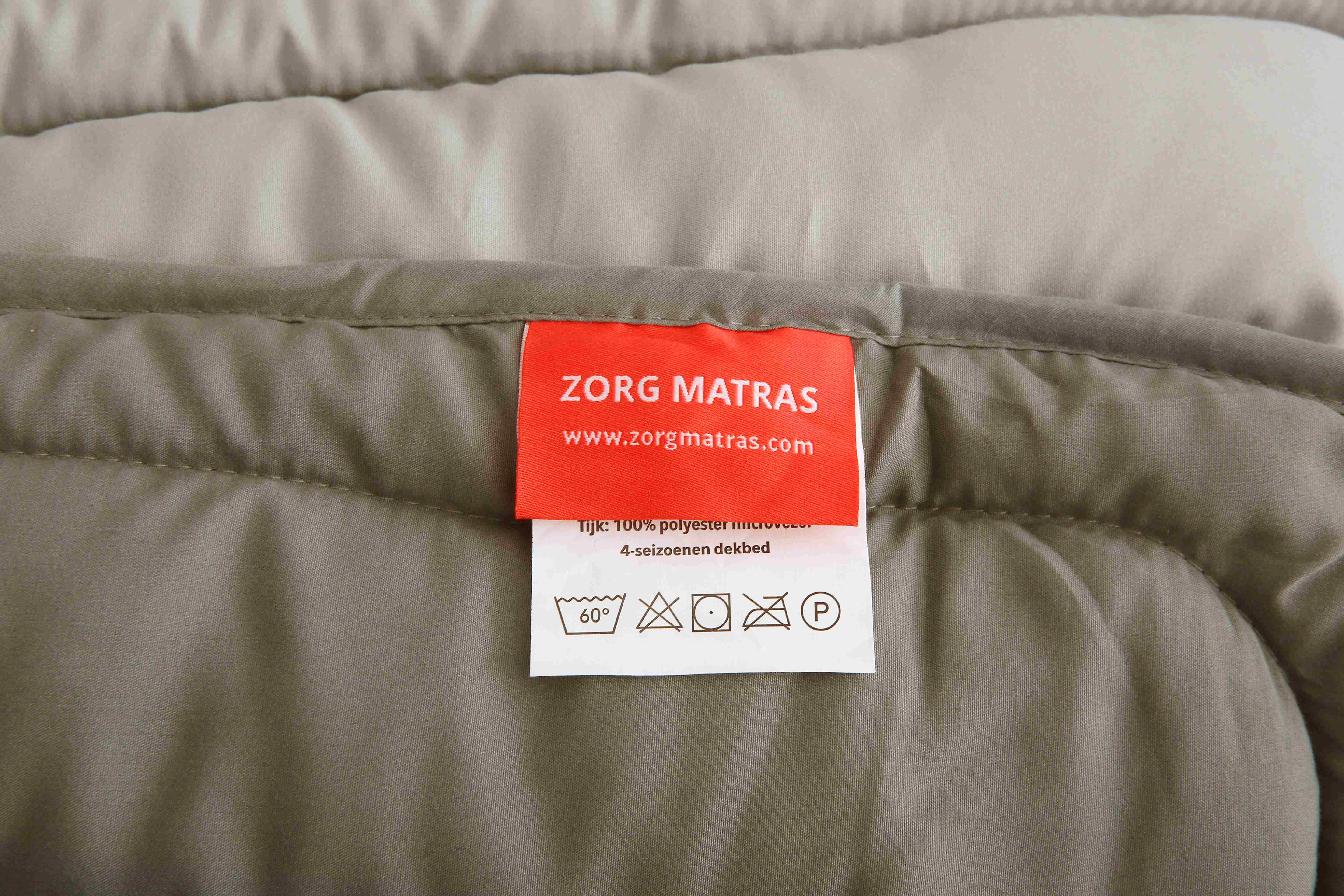 Close-up van het waslabel en wasvoorschriften van het taupe 4-seizoenen dekbed van Zorgmatras