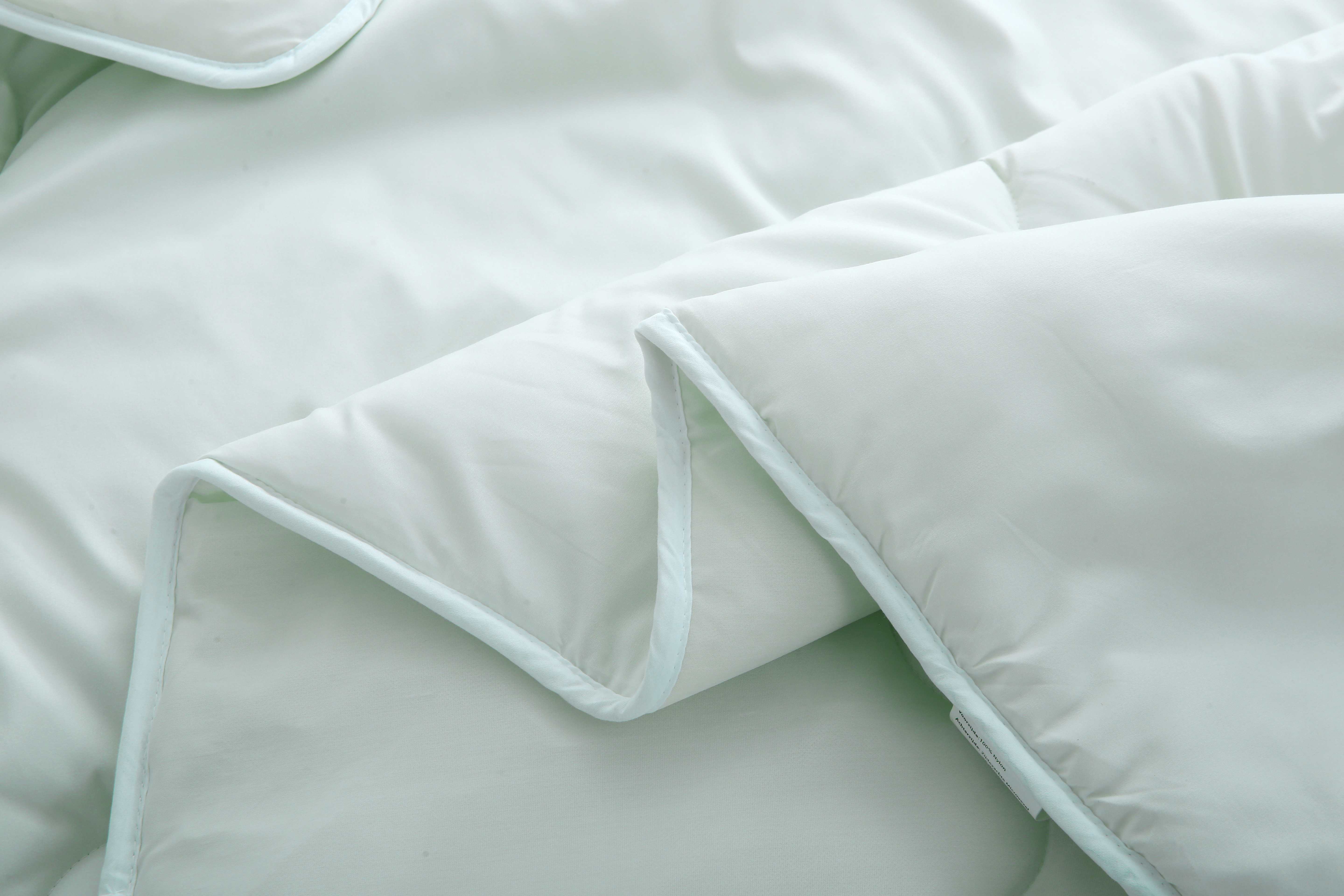 Close-up van de randafwerking van een lichtgroen dekbed zonder overtrek met zachte microvezelhoes